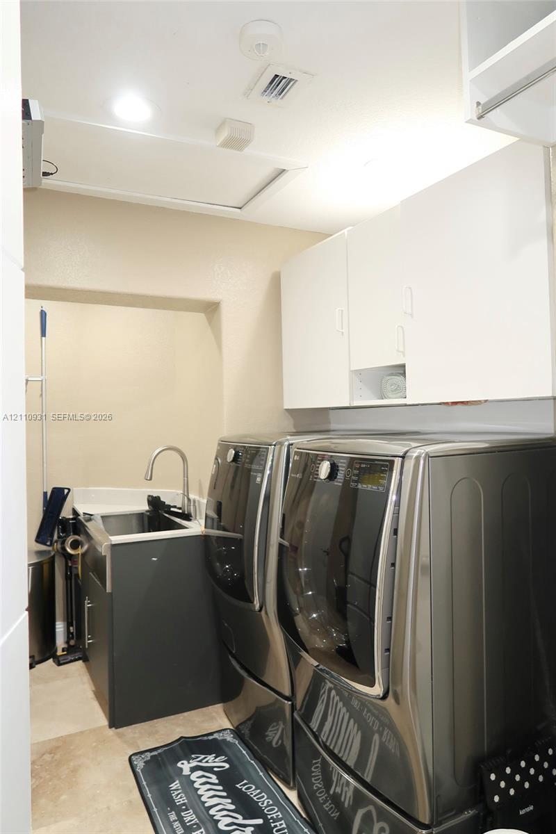 Utility space featuring white overhead cabinetry, stone-finish countertops, an under-mount sink with a high-arch faucet, and neutral tile flooring