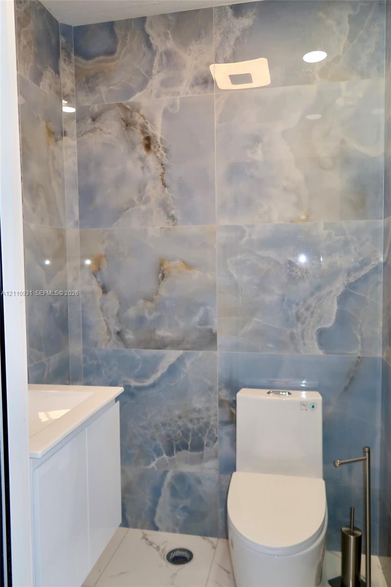 Full-height polished stone wall tile with blue veining, white vanity with integrated sink, and dual-flush toilet