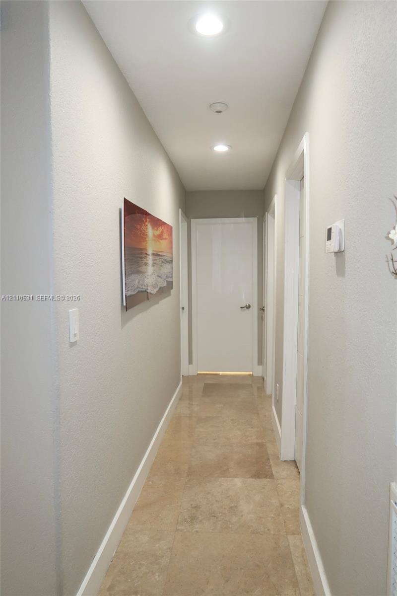 Hallway featuring large-format tile flooring, recessed ceiling lighting, and crisp white interior doors