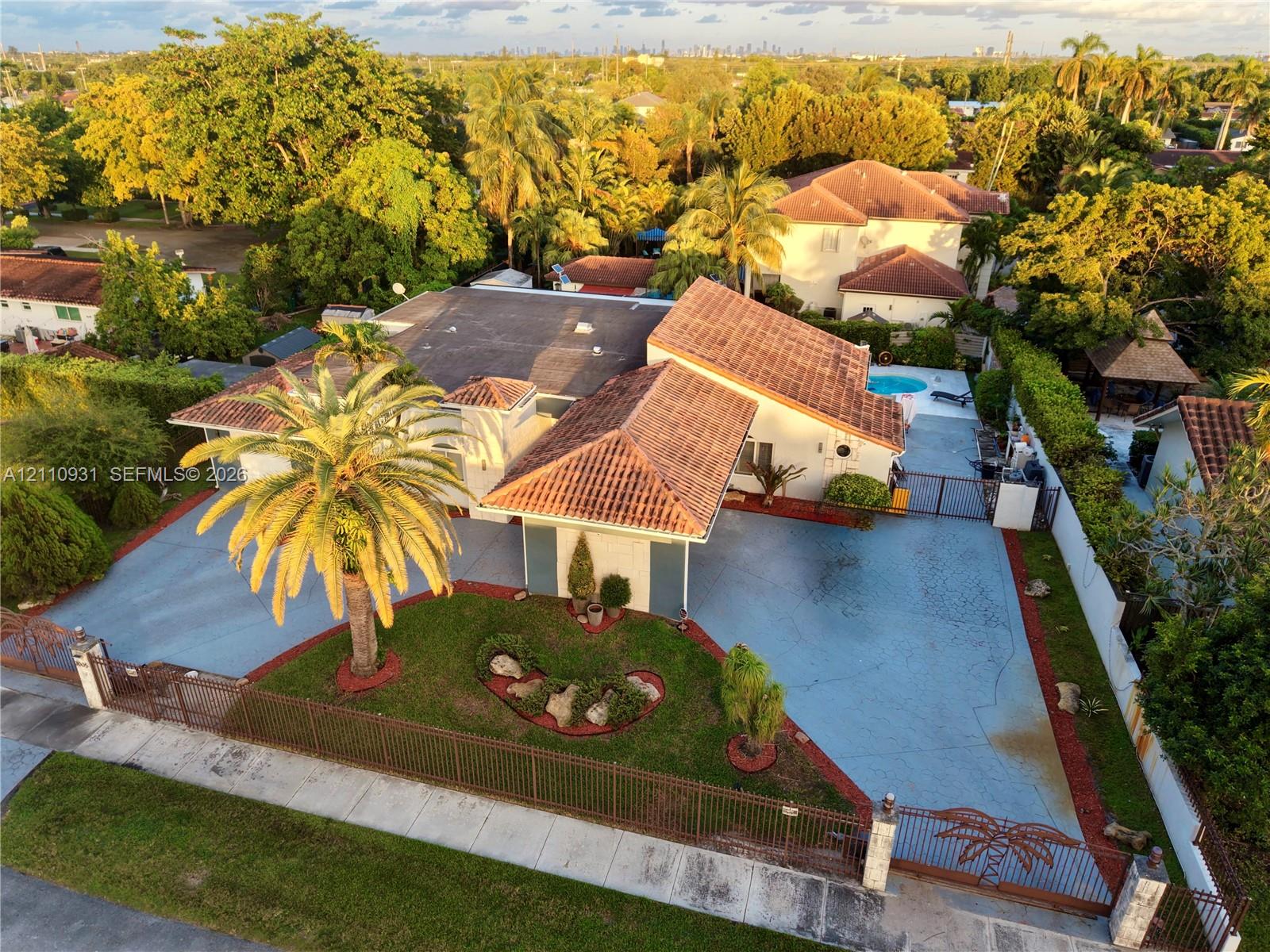 Aerial perspective of a property featuring a tile roof, paved driveway, gated entry, mature landscaping, and an outdoor swimming pool