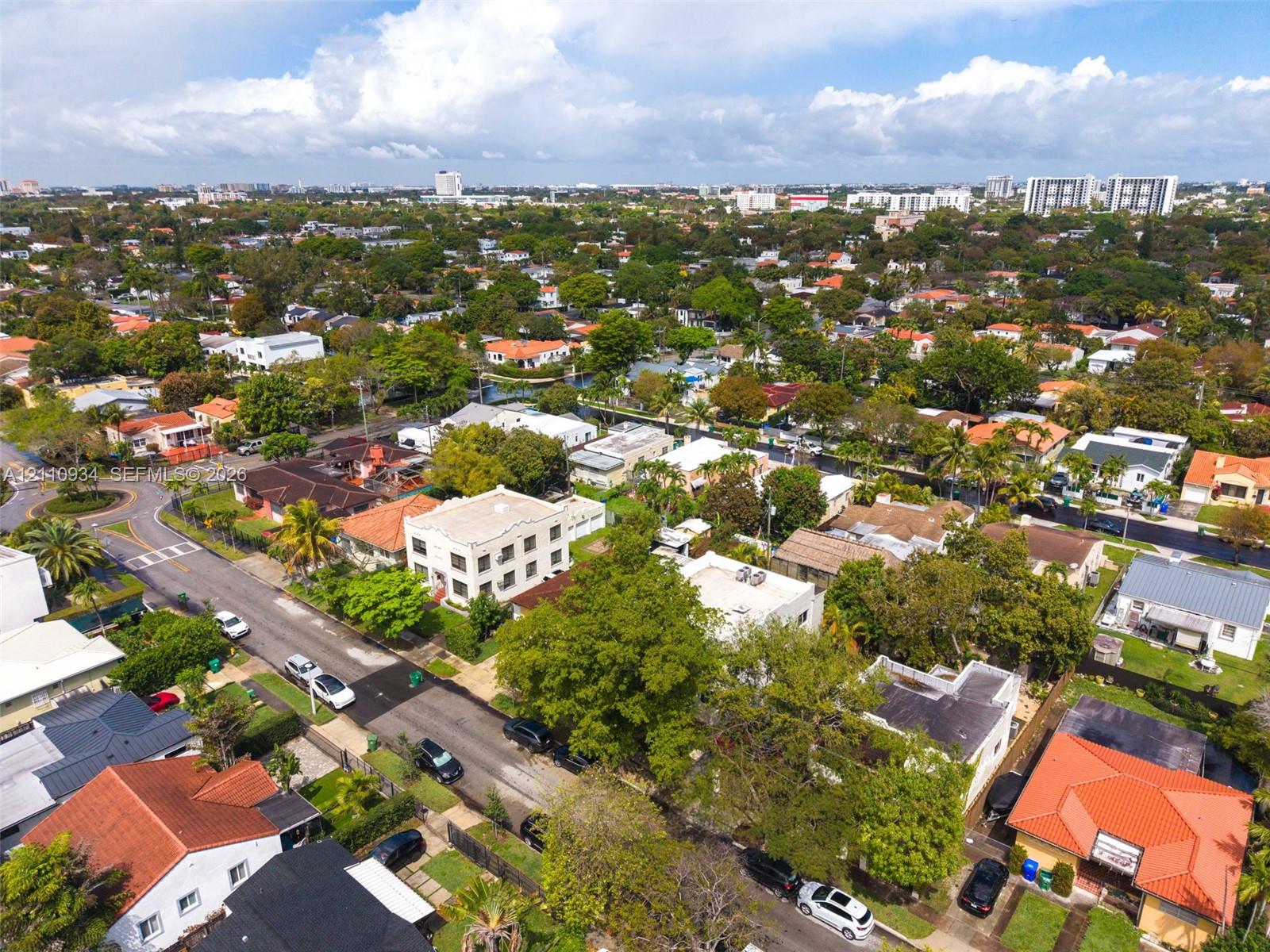 Aerial perspective of a multi-story residential structure featuring a flat roofline, stucco exterior, and multi-paned windows, situated within a dense urban landscape characterized by mature trees and established street grids Aerial perspective of a multi-story residential structure featuring a flat roofline, stucco exterior, and multi-paned windows, situated within a dense urban landscape characterized by mature trees and established street grids