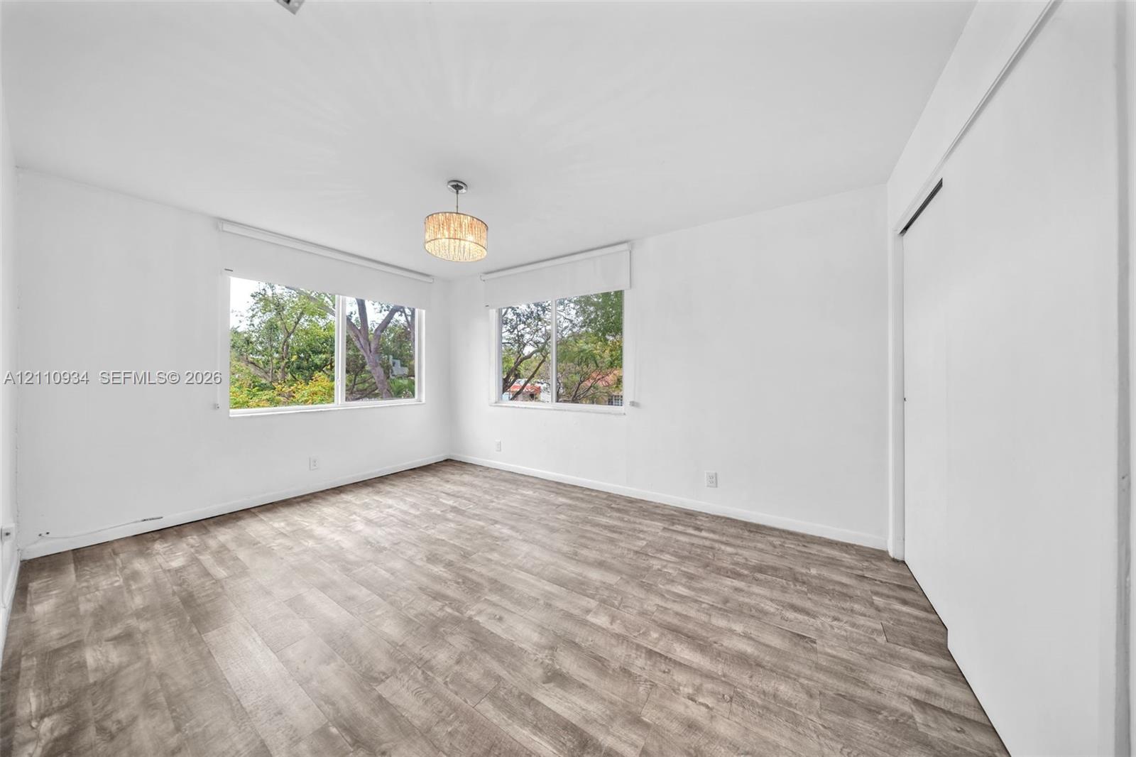 Wood-finish flooring, dual windows with roller shades, and a drum-style ceiling fixture