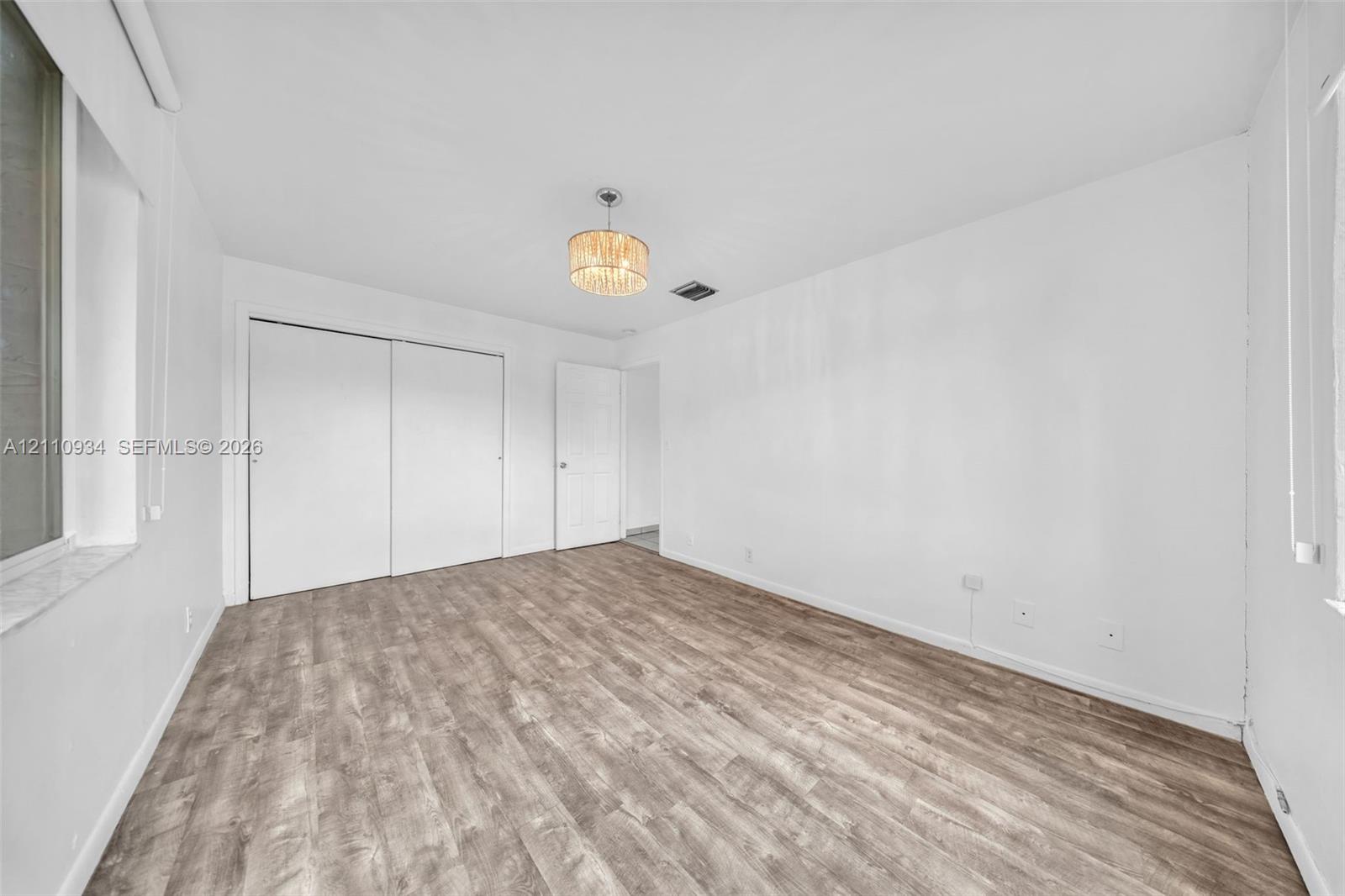 Room featuring wood-finish flooring, a drum-style pendant light fixture, and floor-to-ceiling closet with sliding doors