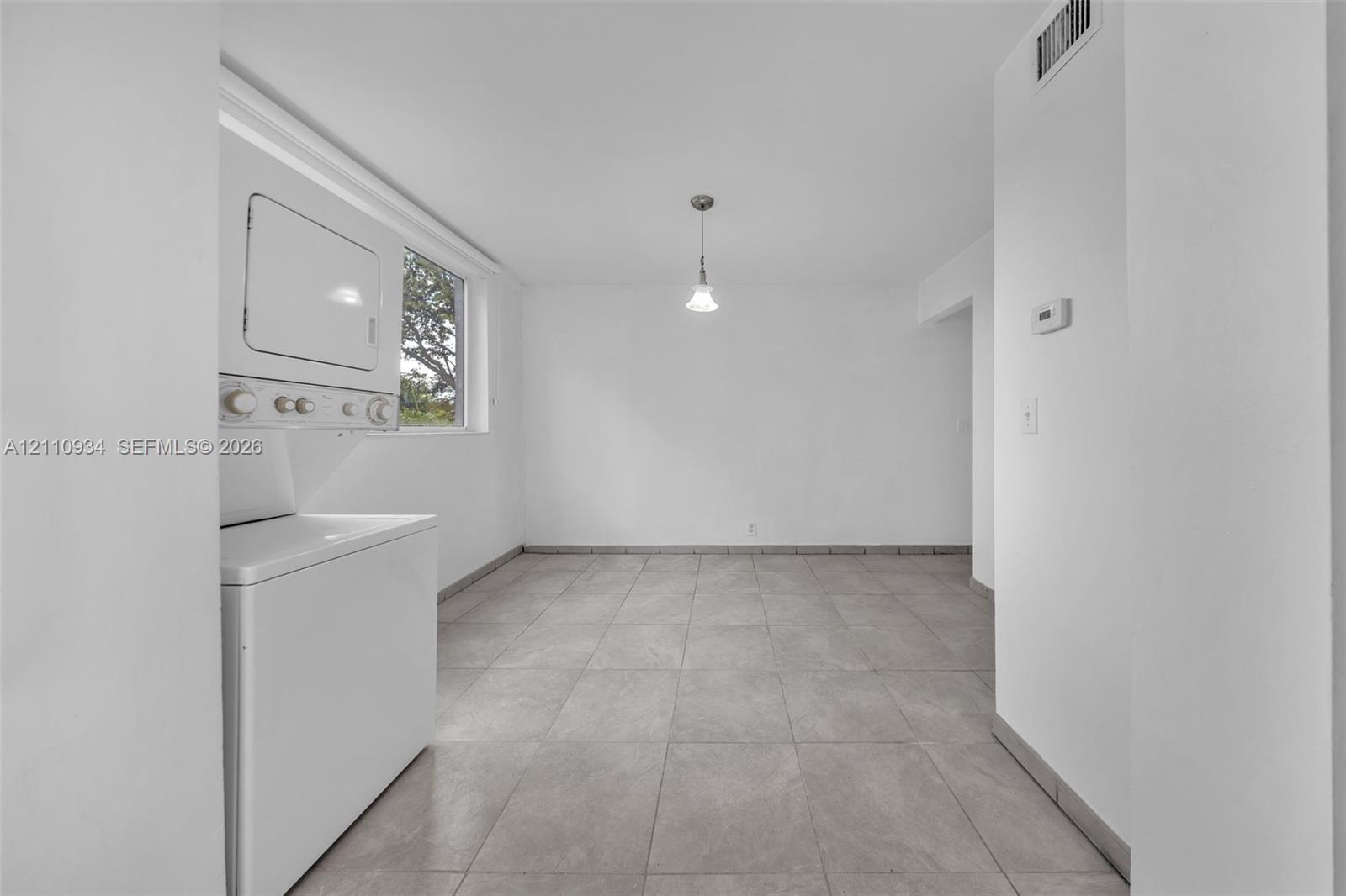 Neutral-toned tile flooring, stacked laundry unit, single-pendant ceiling fixture, and large rectangular window