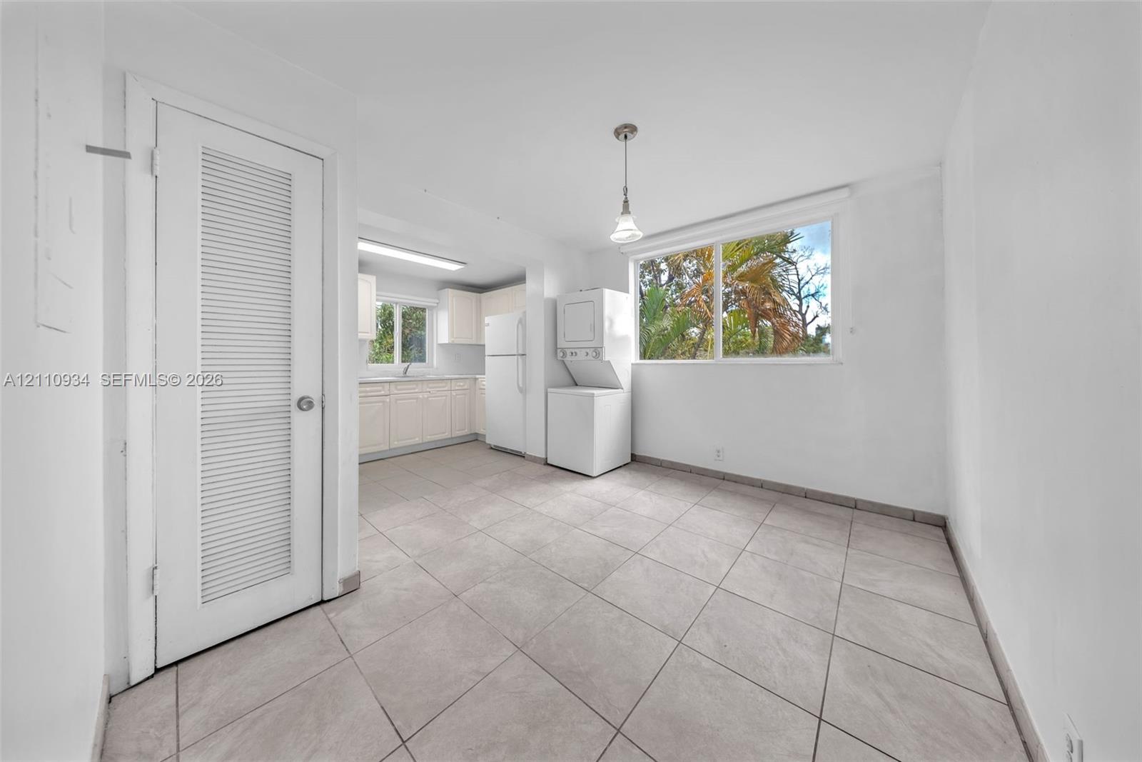 Large-format tile flooring, louvered-panel closet door, white cabinetry, integrated laundry appliances, and expansive picture window