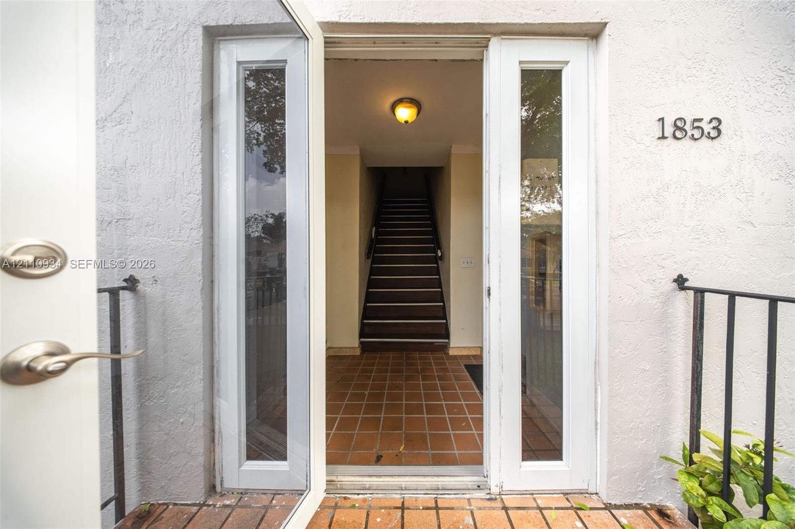 Entryway featuring double glass-paneled doors, terracotta tile flooring, a flush-mount ceiling light fixture, and a black metal handrail