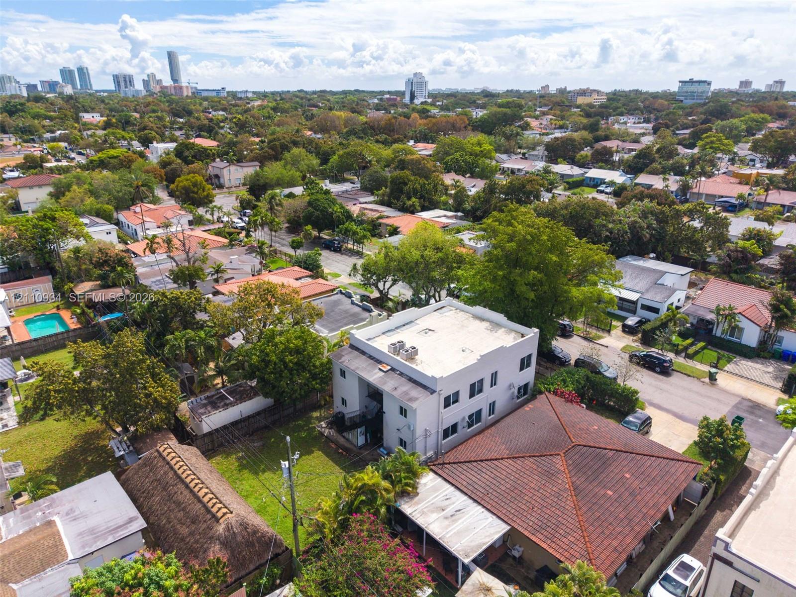 Aerial perspective of a multi-story light-toned stucco building featuring a flat roof and ground-level outdoor space situated within a dense urban landscape