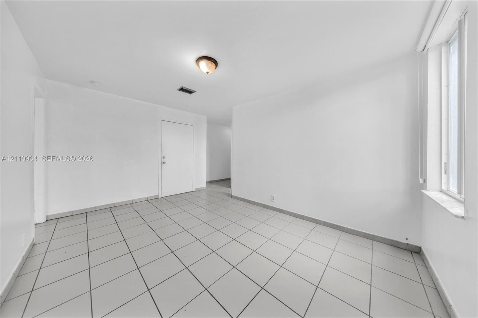 Interior space featuring large-format ceramic tile flooring, neutral white walls, and a recessed window with a stone-finish sill