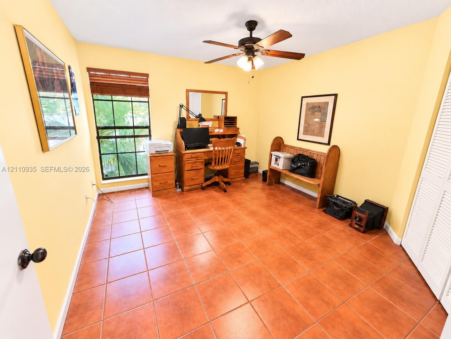 Ceramic tile flooring, multi-pane window with wood-finish blinds, ceiling fan with integrated light fixture, and louvered closet doors