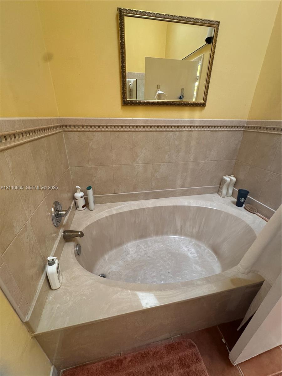 Oval soaking tub with a tiled surround, decorative chair rail tile accent, and wall-mounted metallic fixtures, complemented by a rectangular wall-mounted mirror