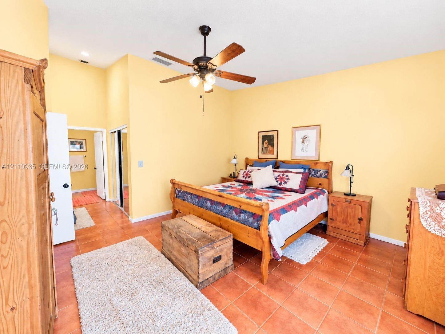 Spacious room featuring high ceilings, square ceramic tile flooring, a multi-blade ceiling fan with integrated lighting, and mirrored closet doors