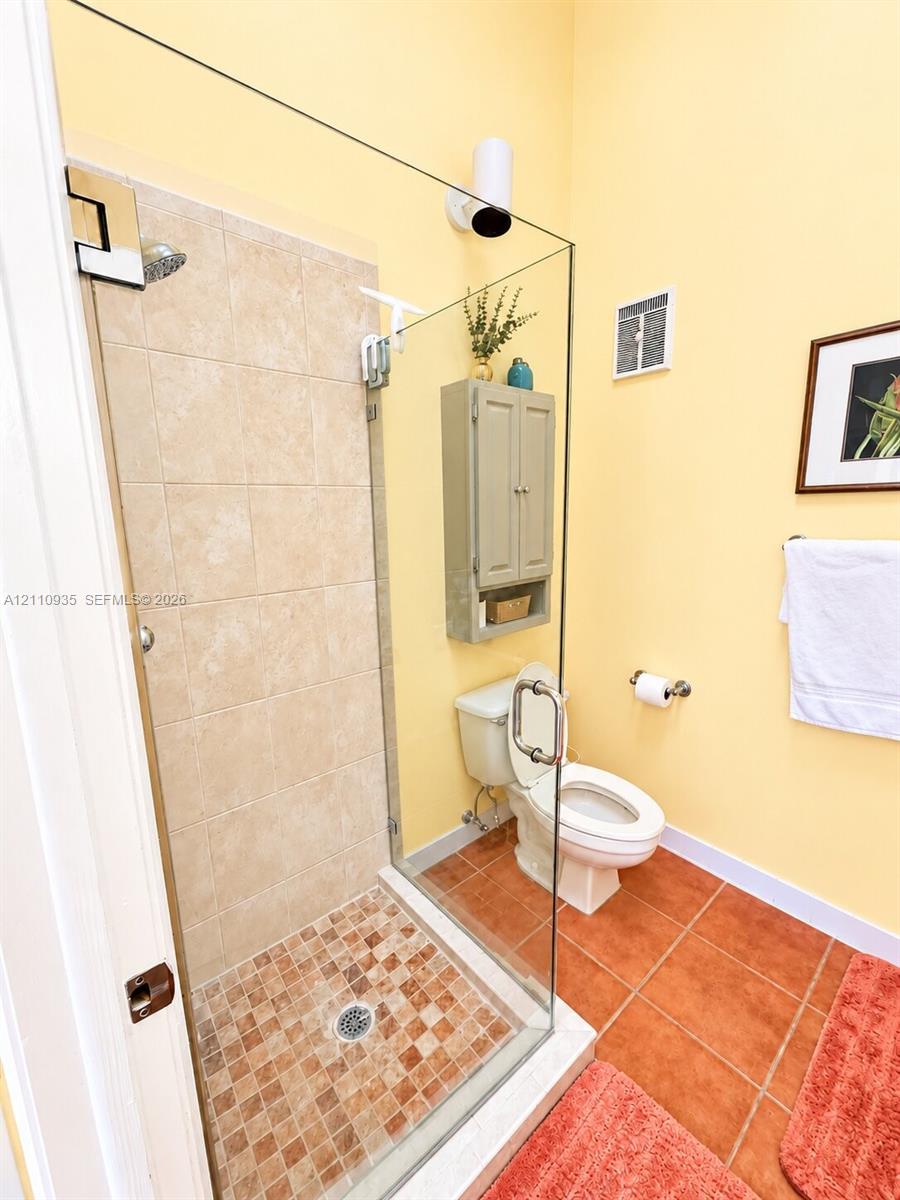 Frameless glass shower enclosure with ceramic wall tile and mosaic floor tiling, accompanied by a wall-mounted storage cabinet