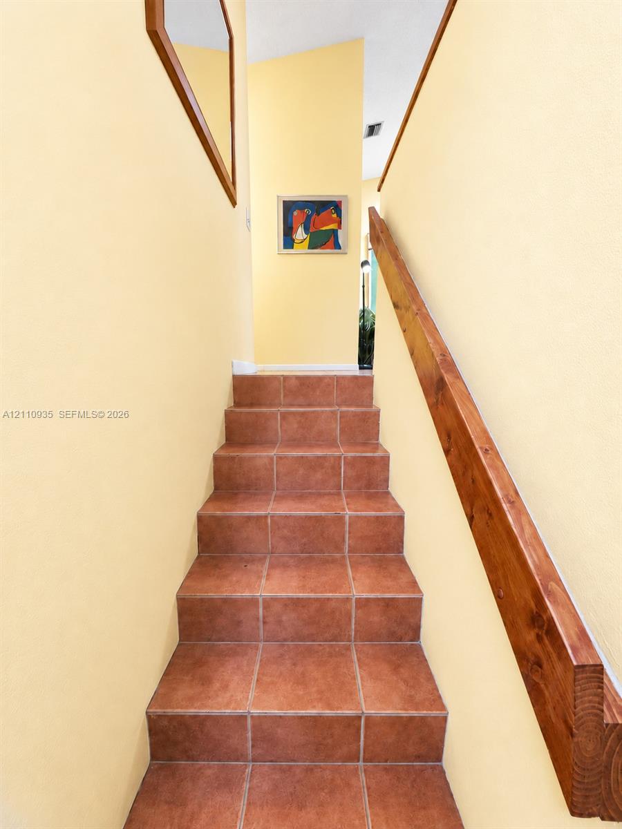 Staircase featuring terracotta-style tile treads and a solid wood handrail