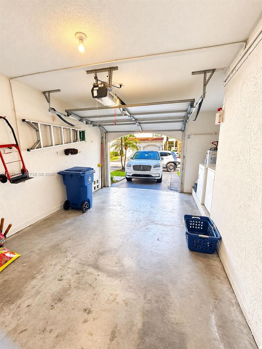 Enclosed one-car garage featuring a concrete floor, automated overhead garage door system, and textured wall finish