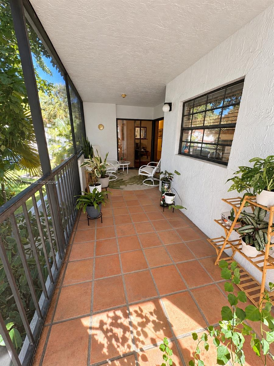 Screened-in porch featuring terracotta tile flooring, textured stucco walls, and black-framed metal railings