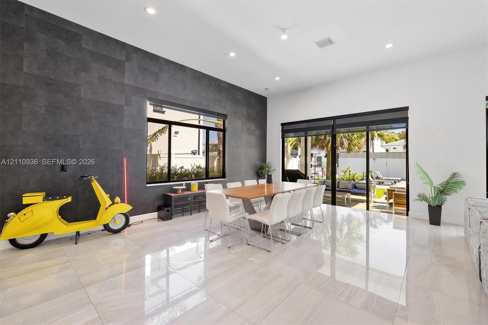 Living area featuring high ceilings, large-format tile flooring, a charcoal-toned accent wall, and sliding glass doors leading to the exterior Living area featuring high ceilings, large-format tile flooring, a charcoal-toned accent wall, and sliding glass doors leading to the exterior
