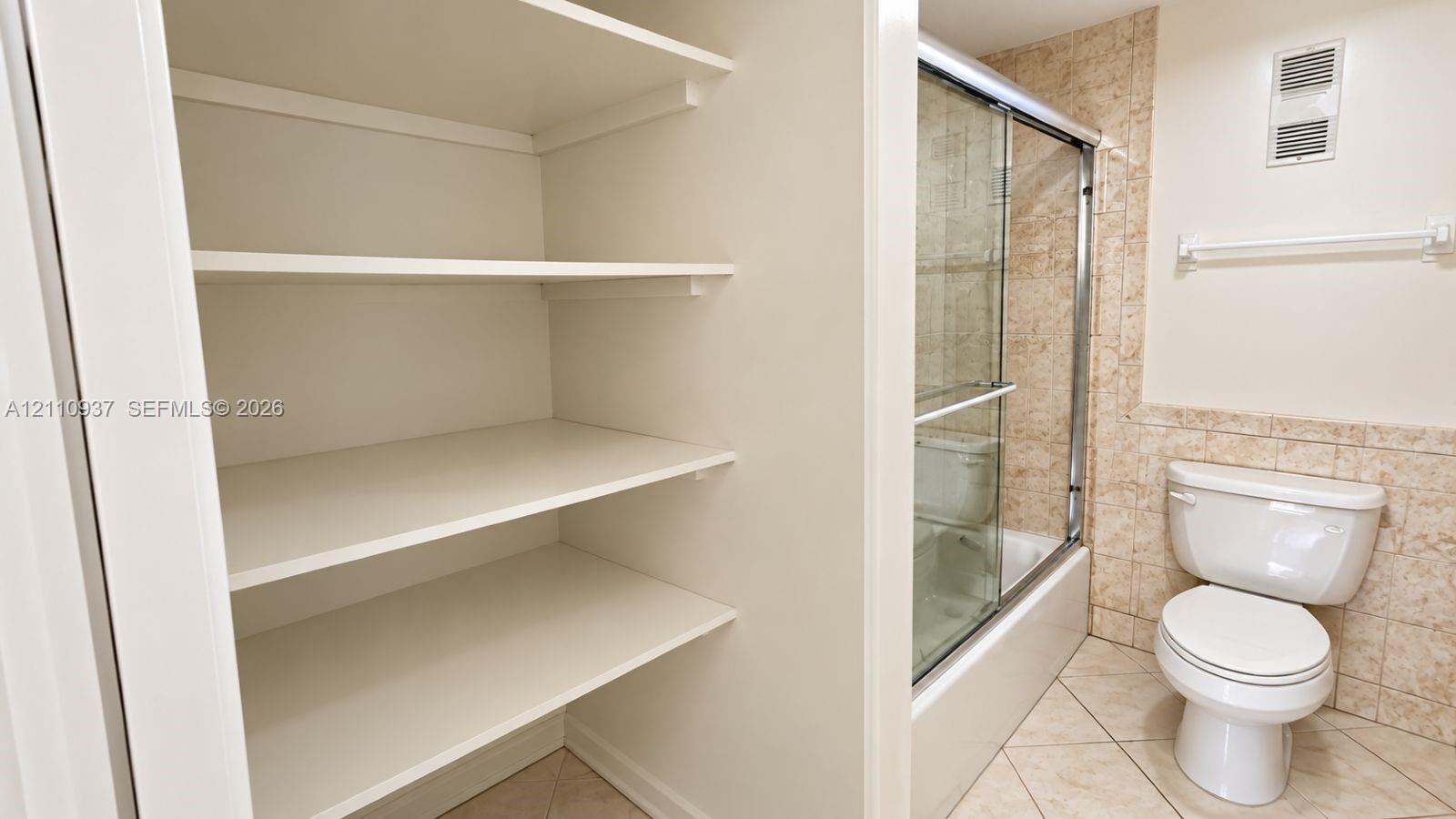 Built-in storage shelving, walk-in shower with a sliding glass door, ceramic tile surround, and tile flooring