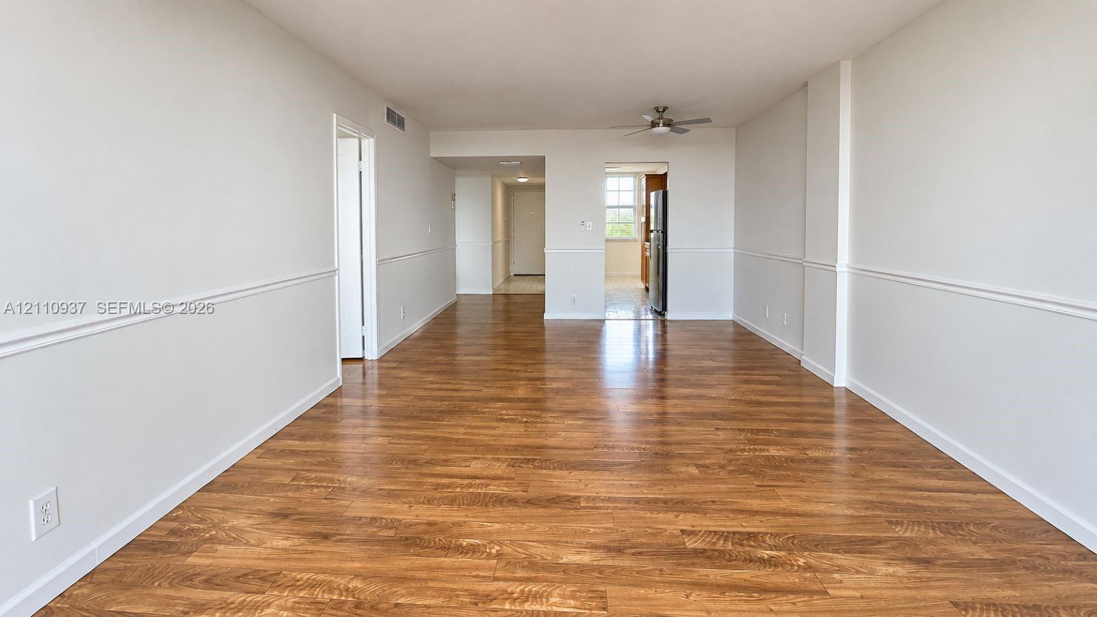 Open-concept interior featuring wood-finish flooring, chair rail molding, and a ceiling-mounted fan