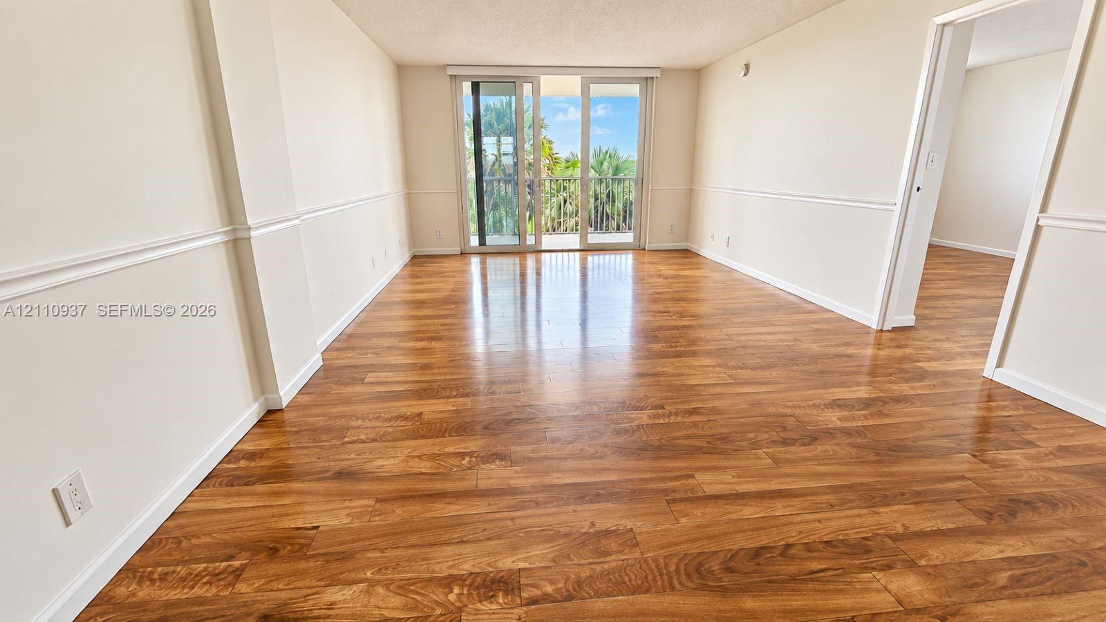 Interior living area featuring wood-finish flooring, chair rail molding, and sliding glass doors opening to a balcony