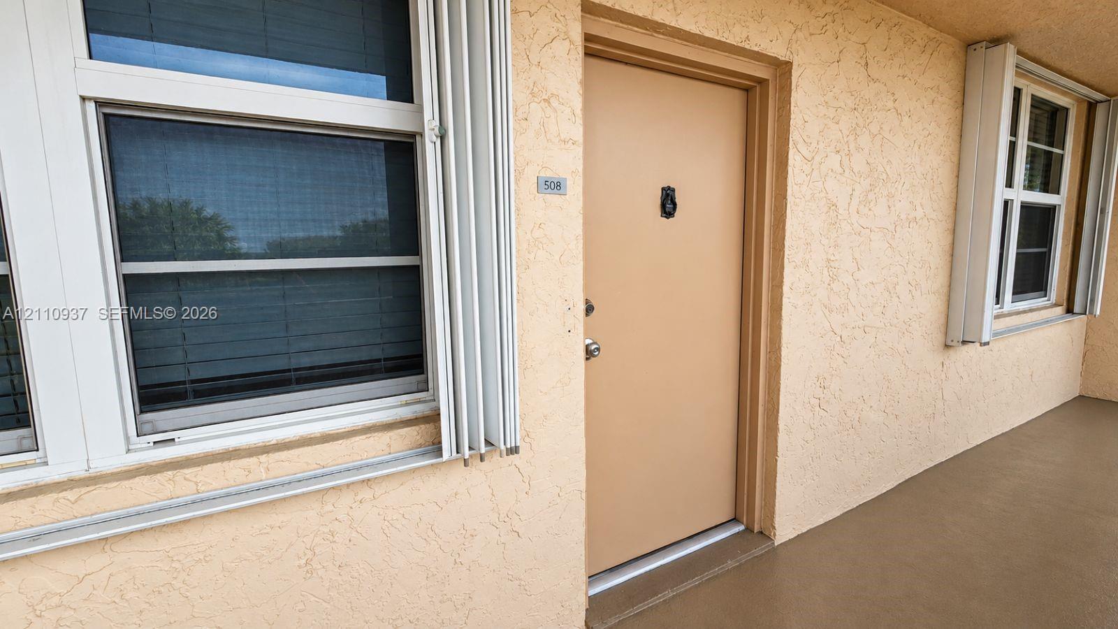 Exterior entrance featuring textured stucco siding, accordion-style hurricane shutters, and a solid-core door with metal hardware