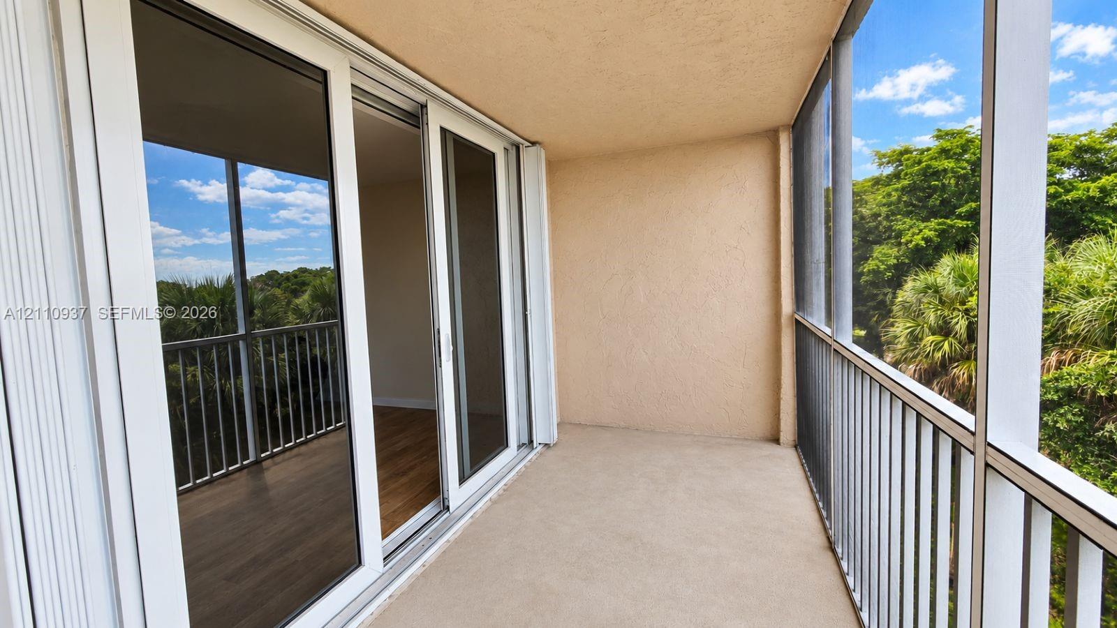 Covered balcony featuring a screened-in enclosure, white metal railing, and sliding glass door entry