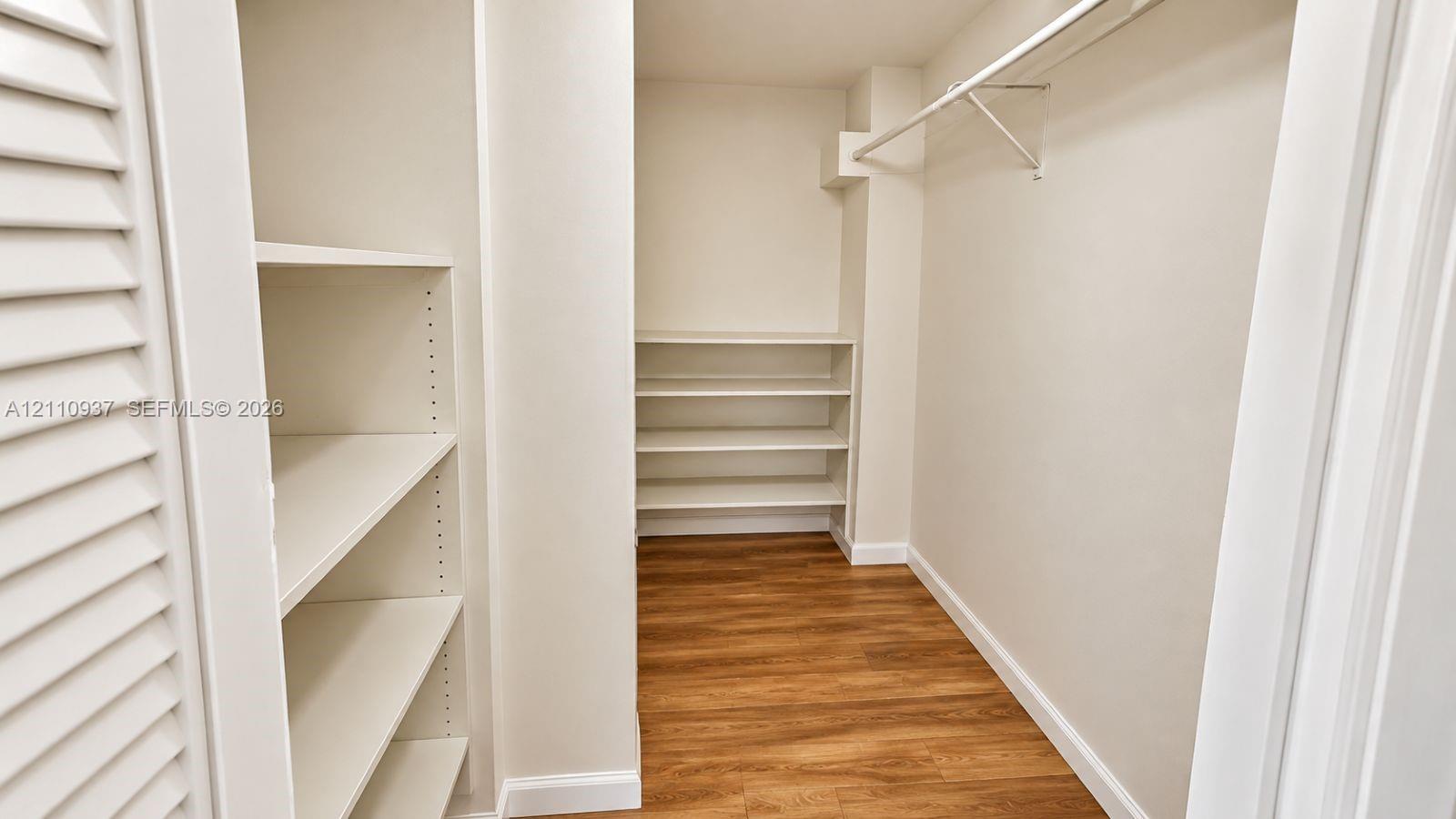 Walk-in storage space featuring wood-finish flooring, white adjustable shelving, and an integrated hanging rod