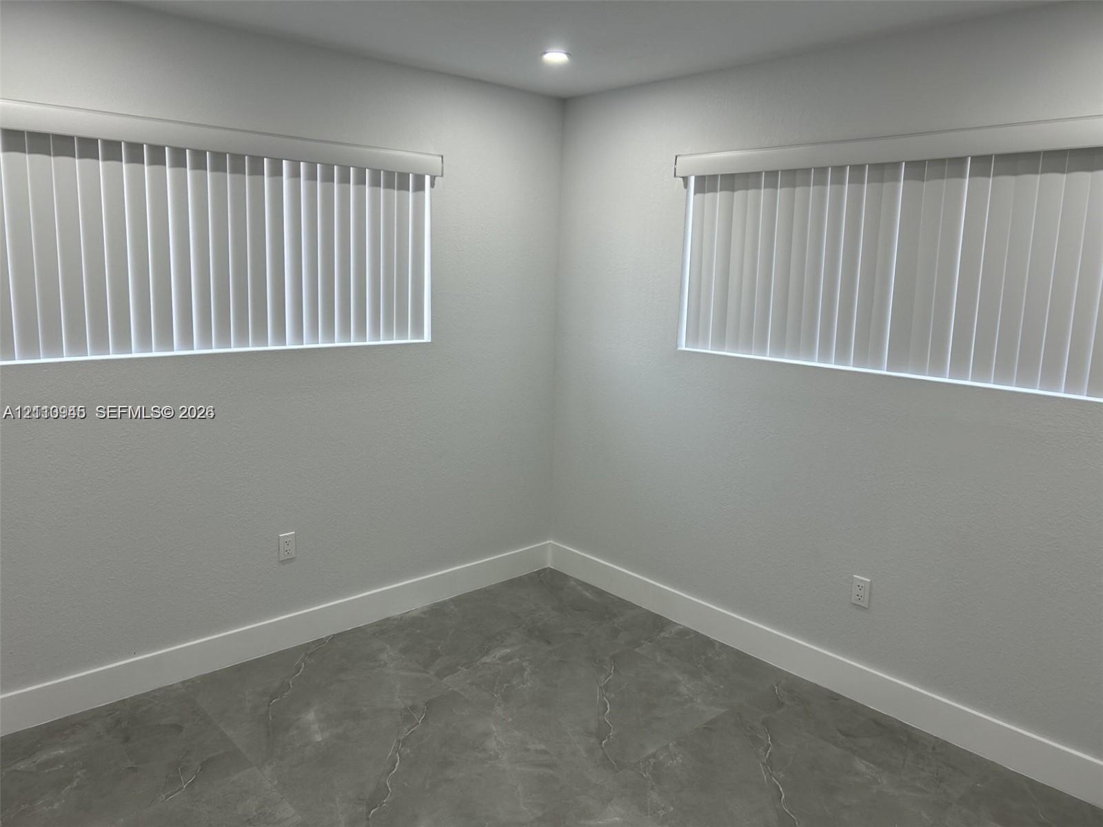 Neutral-toned interior featuring large-format tile flooring, recessed ceiling lighting, and two windows equipped with vertical blinds