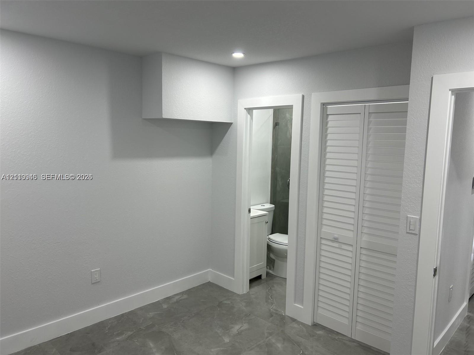 Neutral-toned interior space featuring light grey ceramic tile flooring, recessed ceiling lighting, and white louvered closet doors