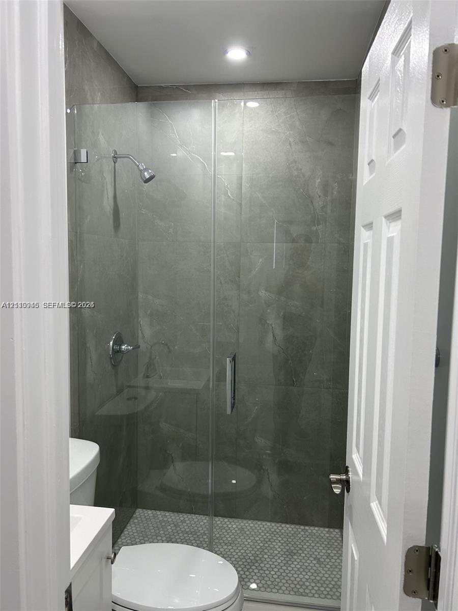 Walk-in shower featuring large-format stone-finish tile surround, frameless glass enclosure, recessed ceiling lighting, and mosaic tile shower floor