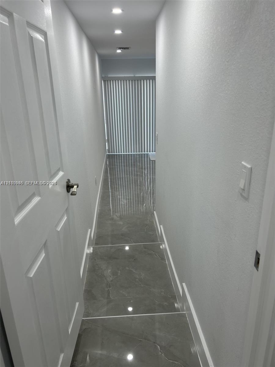 Hallway featuring large-format grey tile flooring, recessed ceiling lighting, and vertical blinds over a sliding glass door