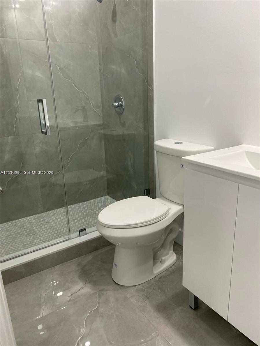 Walk-in shower with large-format tile surround, glass enclosure, mosaic tile floor, white vanity cabinet, and modern polished chrome fixtures