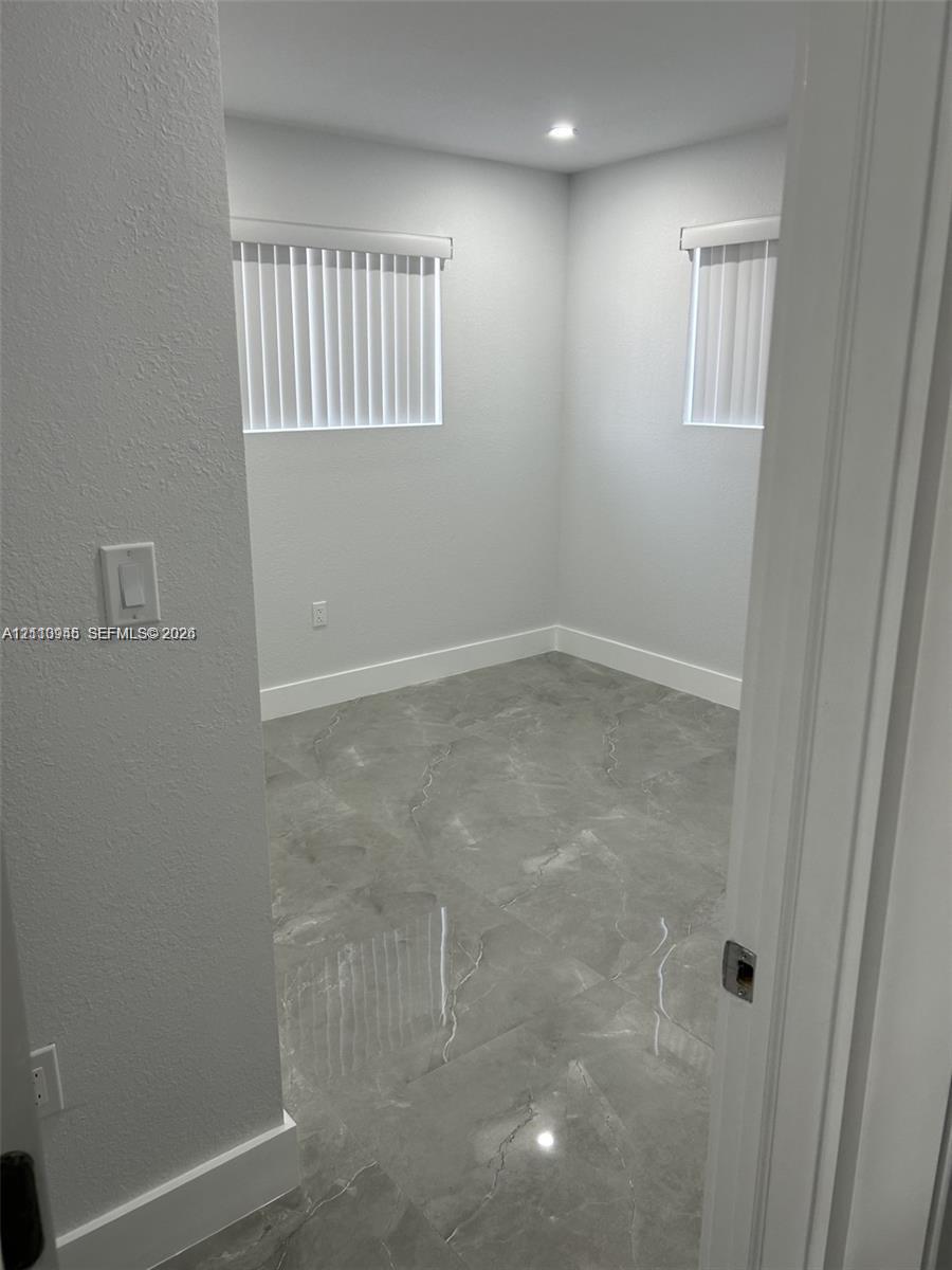 Interior space featuring large-format grey stone-finish tile flooring, neutral walls, two windows with vertical blinds, and recessed lighting