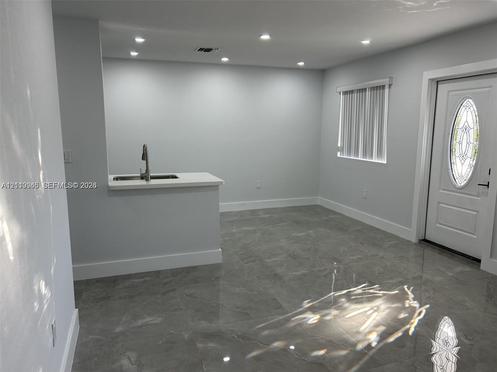 Large-format stone-finish tile flooring, recessed ceiling lighting, pass-through counter with a stainless steel sink, and an exterior door with an oval decorative glass insert