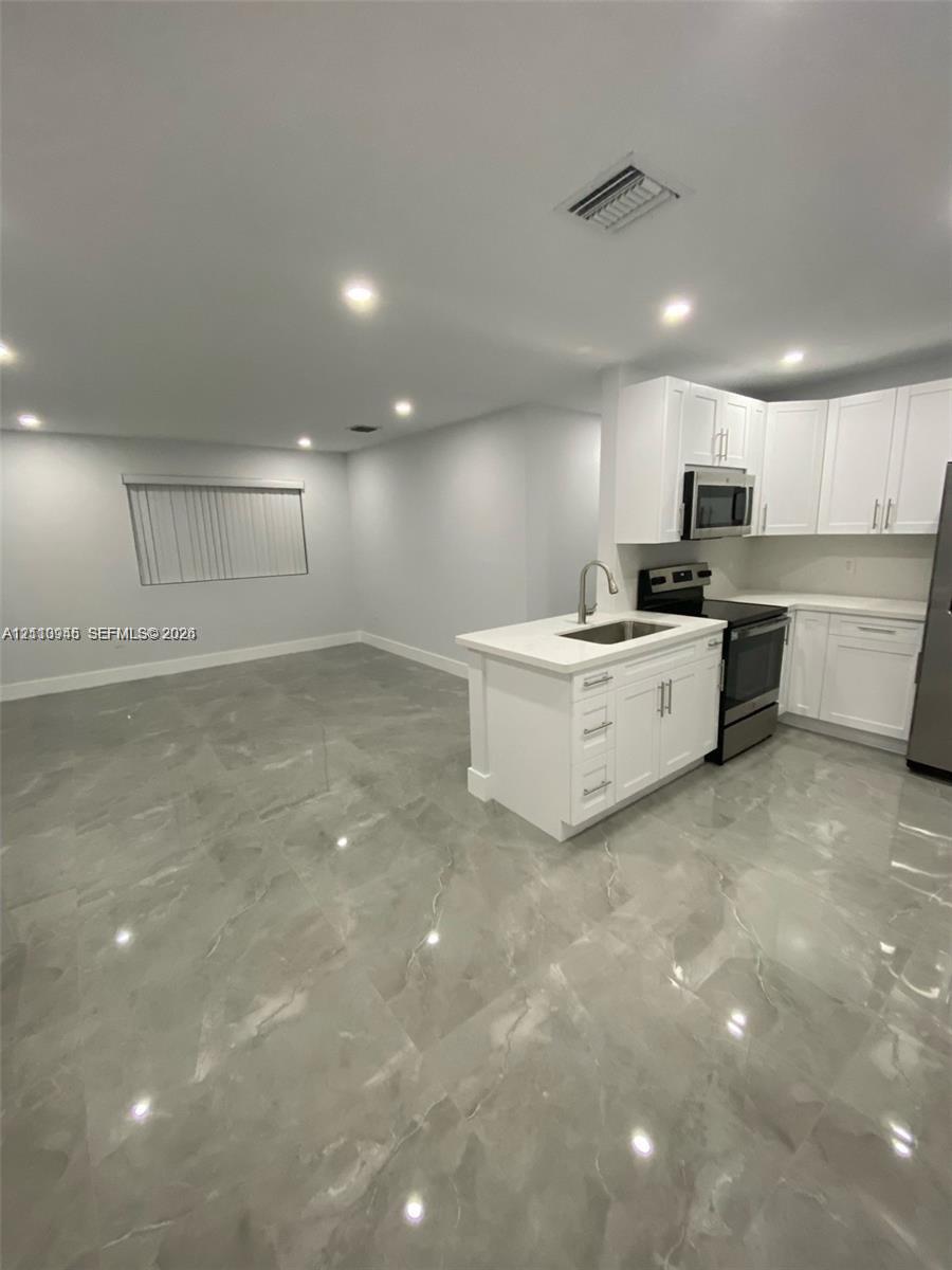 Kitchen area featuring white shaker-style cabinetry, a central island with an undermount sink, recessed lighting, and large-format porcelain tile flooring