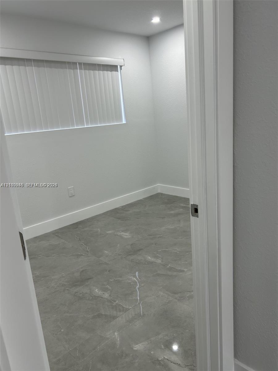 Interior space featuring large-format grey tile flooring, neutral wall tones, recessed lighting, and a horizontal window with vertical blinds