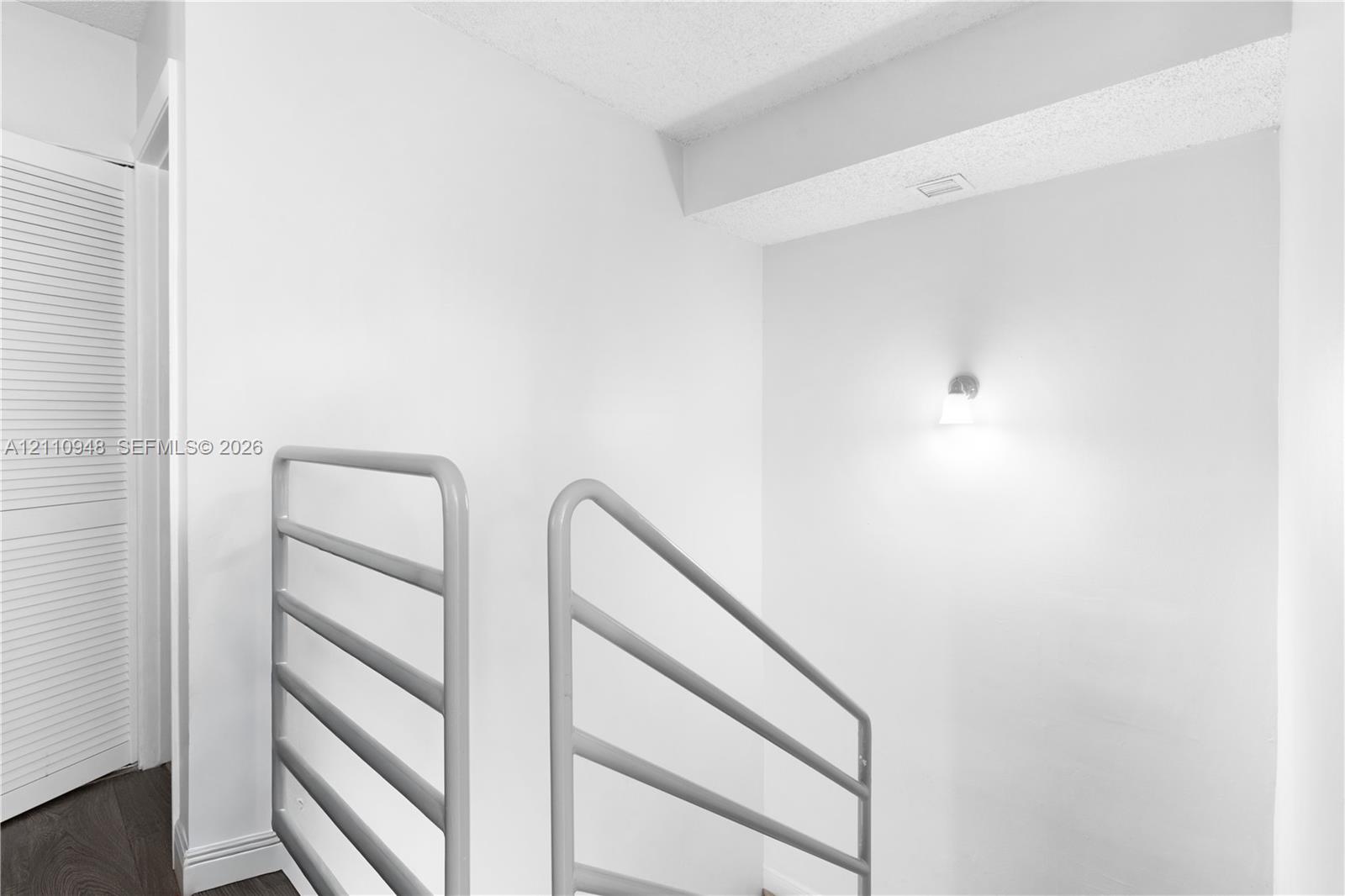 Horizontal metal stair railing, neutral wall finish, and wall-mounted light fixture