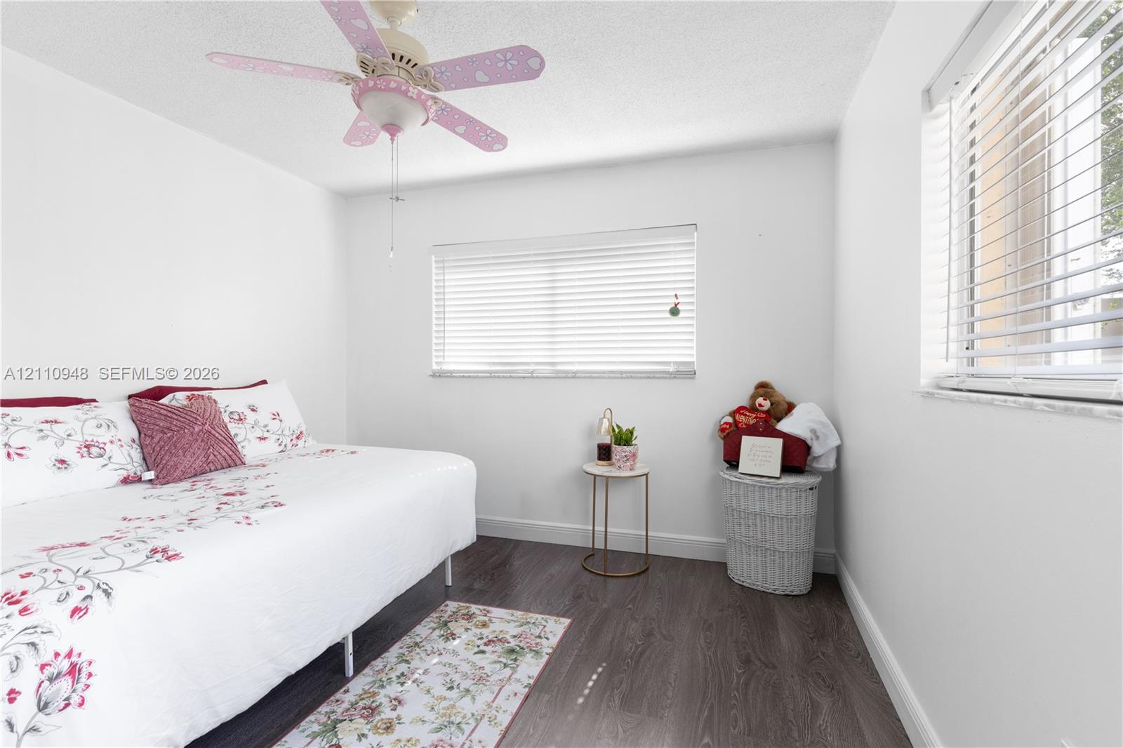 Neutral-toned interior featuring wood-finish flooring, dual windows with horizontal blinds, and a ceiling-mounted light fixture