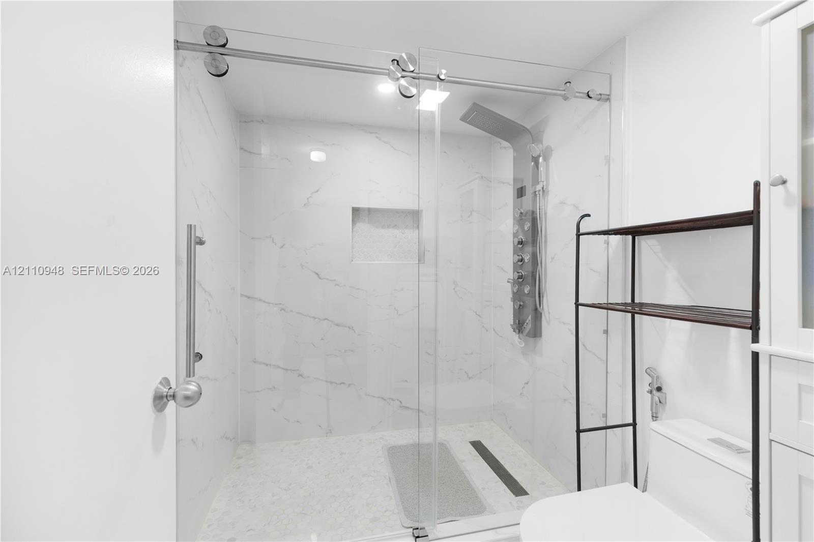 Walk-in shower featuring a sliding glass door, floor-to-ceiling stone-patterned wall tile, recessed niche, and integrated rainfall shower panel with body sprayers