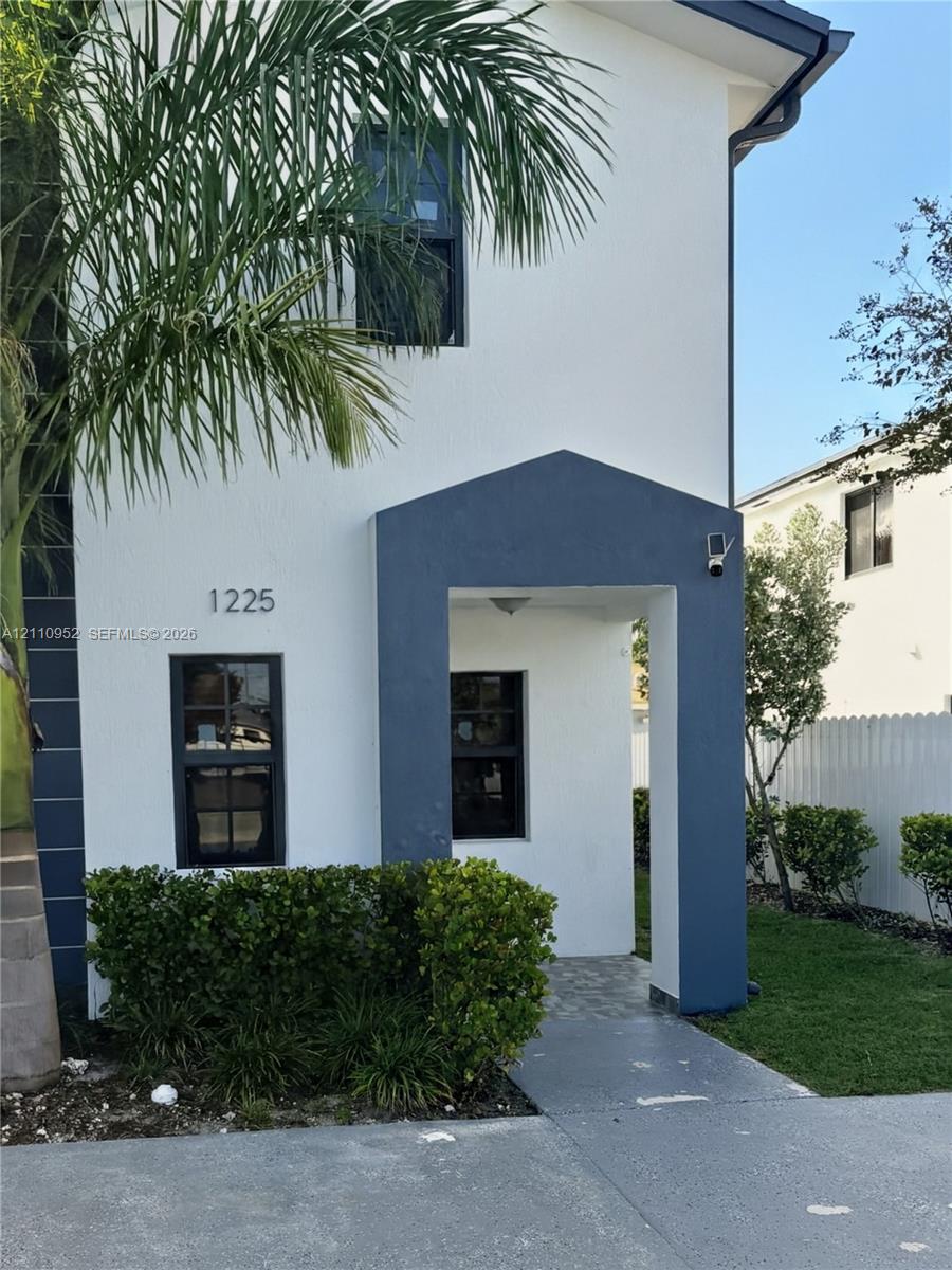 Stucco exterior featuring contrasting trim, a covered entryway, multi-pane windows, and concrete driveway