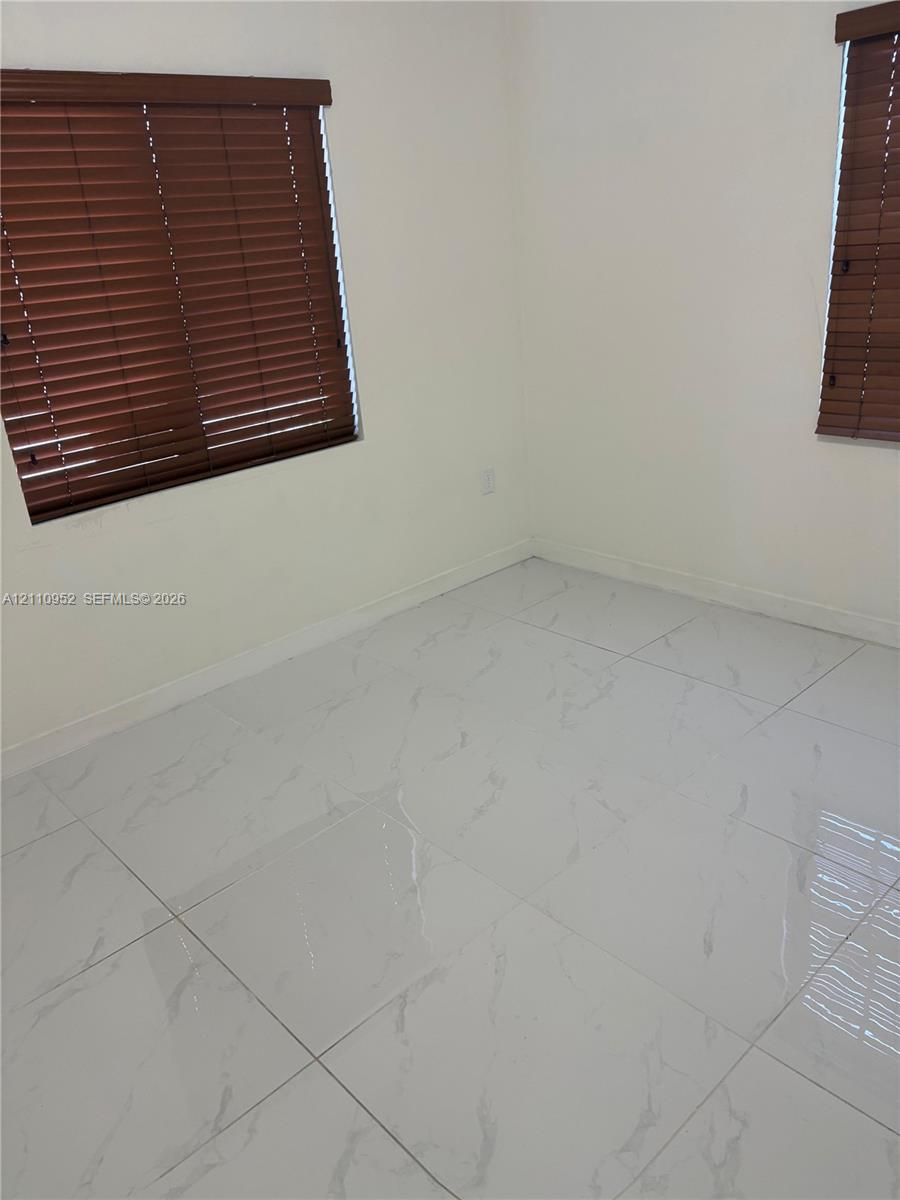Large-format stone-style tile flooring with neutral wall finishes, paired with two windows featuring horizontal wood-finish blinds