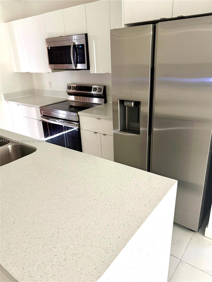 Kitchen featuring white flat-panel cabinetry, stone-finish countertops, stainless steel side-by-side refrigerator, matching stainless steel range, and built-in microwave