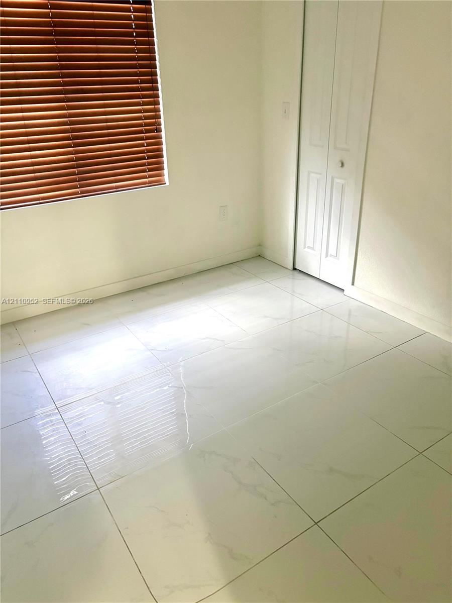 Polished stone-finish tile flooring, white bi-fold closet doors, and horizontal slat window blinds
