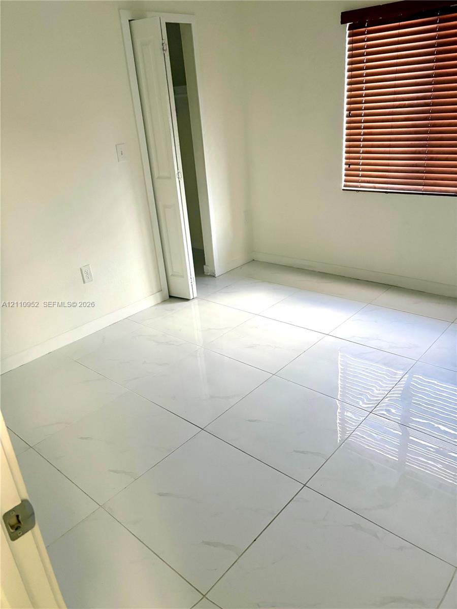 Large-format tile flooring with a light marbled finish, accompanied by a bi-fold closet door and horizontal slat window blinds