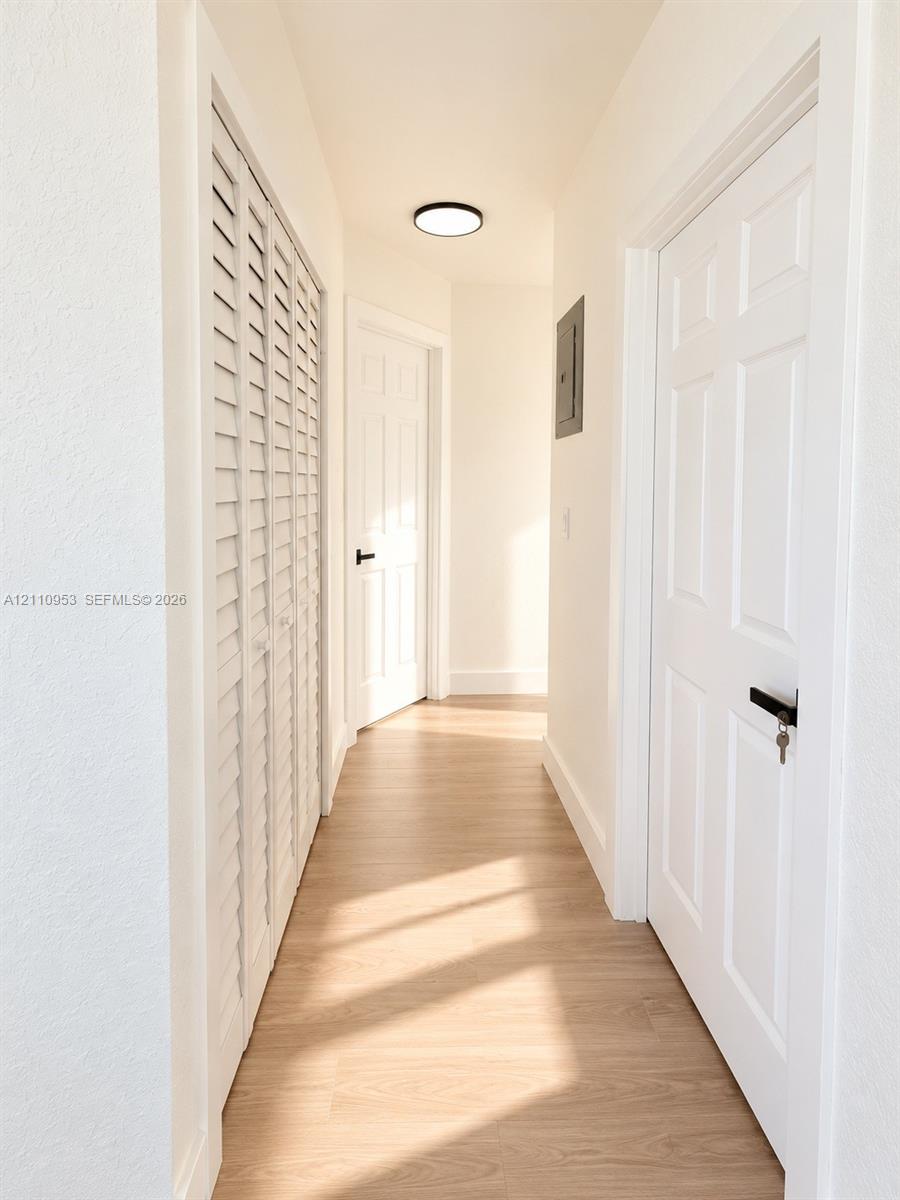 Hallway featuring wood-finish flooring, white six-panel doors with matte black hardware, white louvered closet doors, and a flush-mount circular ceiling fixture