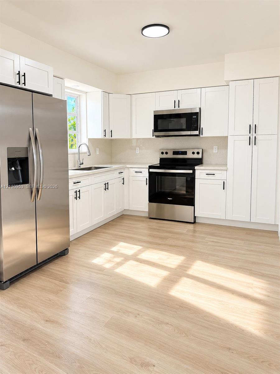 Kitchen featuring white shaker-style cabinetry, stainless steel appliances, light wood-finish flooring, and a single-basin undermount sink with a gooseneck faucet Kitchen featuring white shaker-style cabinetry, stainless steel appliances, light wood-finish flooring, and a single-basin undermount sink with a gooseneck faucet