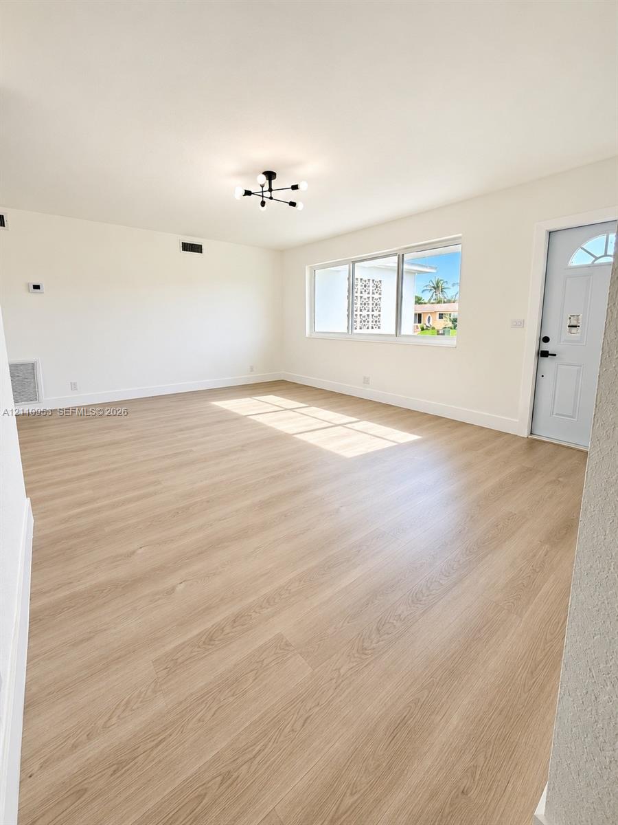 Interior space featuring wood-finish flooring, a modern sputnik-style ceiling light fixture, large windows, and a panelled exterior door with decorative glass inlay Interior space featuring wood-finish flooring, a modern sputnik-style ceiling light fixture, large windows, and a panelled exterior door with decorative glass inlay