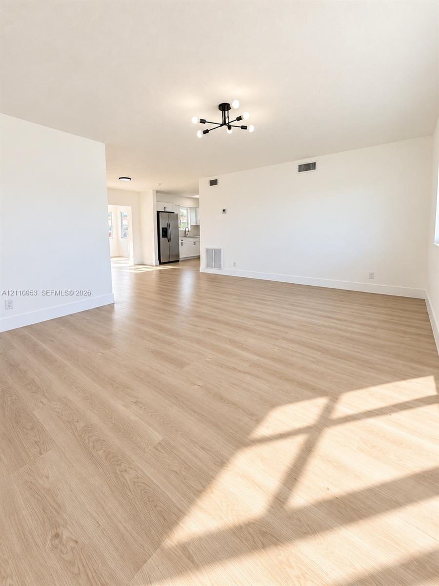 Open-concept interior featuring wood-finish flooring, a contemporary six-arm matte black chandelier, and neutral wall tones Open-concept interior featuring wood-finish flooring, a contemporary six-arm matte black chandelier, and neutral wall tones