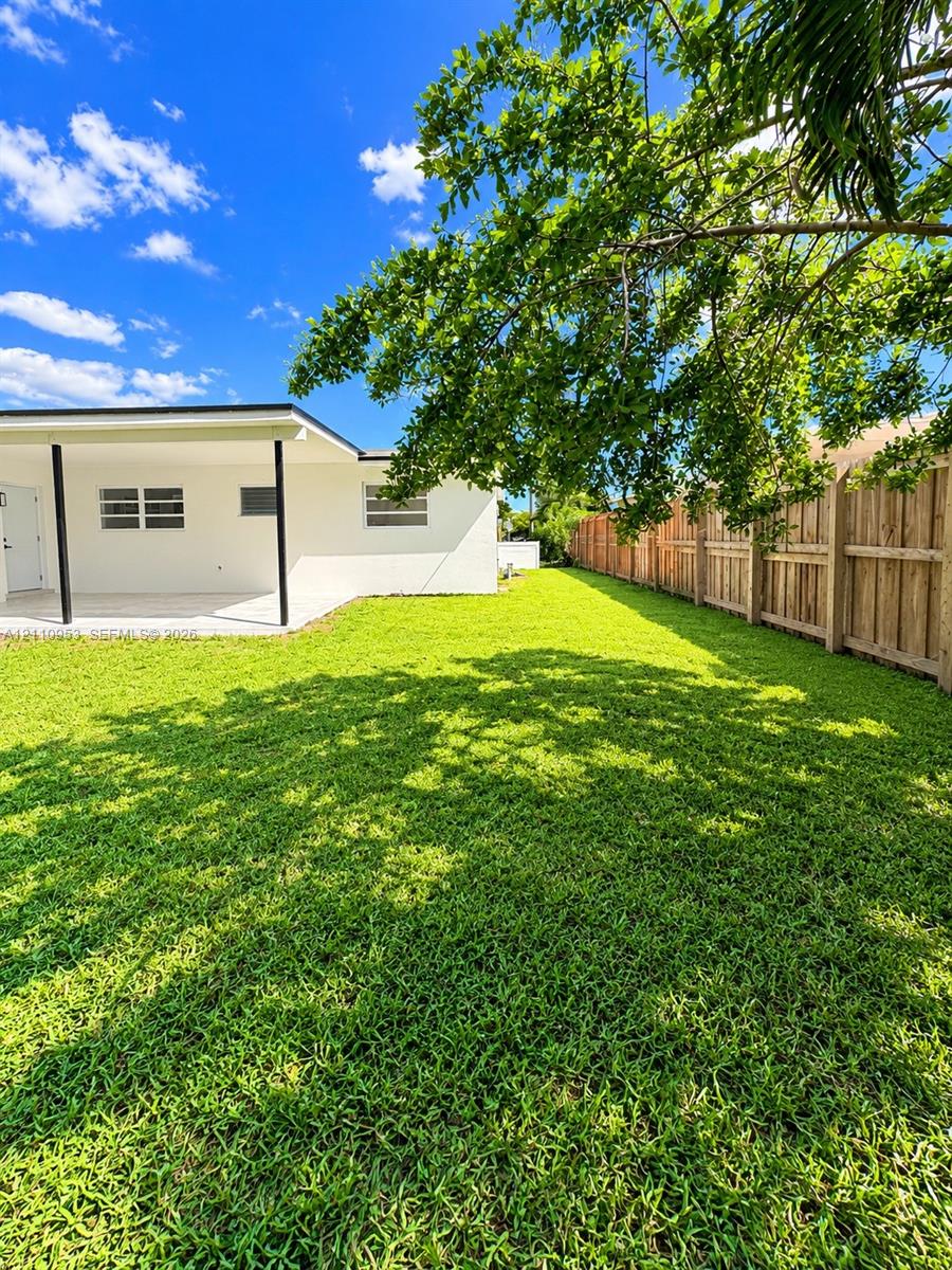 Private backyard featuring a sprawling lawn, wood privacy fencing, and a covered patio with support columns