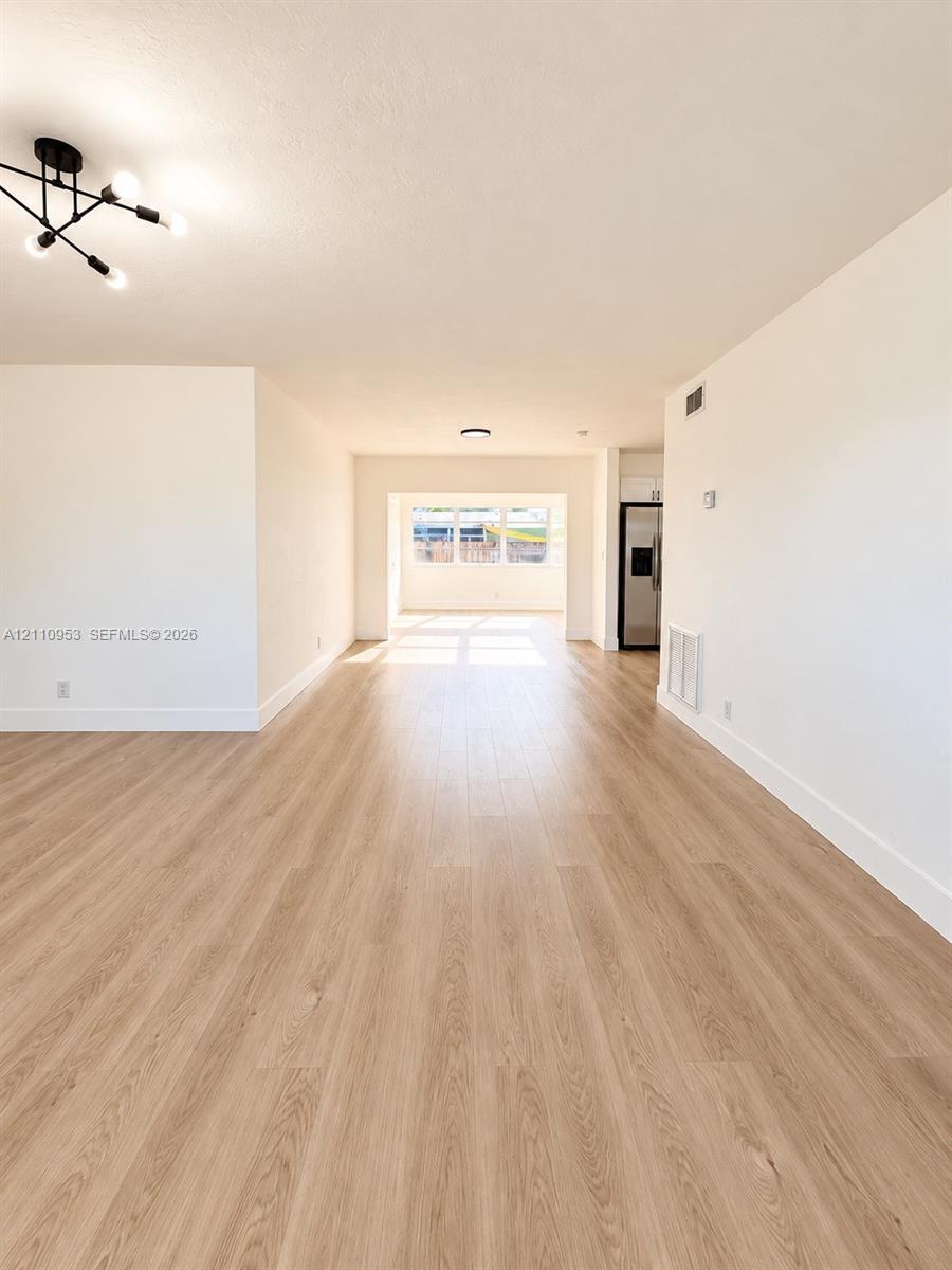 Open floor plan featuring wood-finish flooring, neutral walls, and multi-arm geometric ceiling lighting Open floor plan featuring wood-finish flooring, neutral walls, and multi-arm geometric ceiling lighting