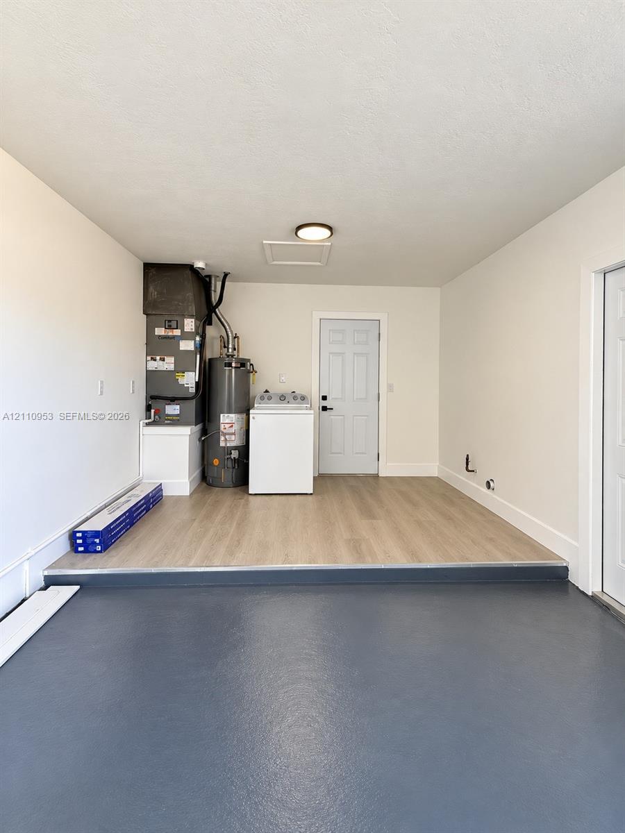 Dedicated utility area featuring wood-finish flooring, a six-panel door, painted walls, and a mounted ceiling light fixture